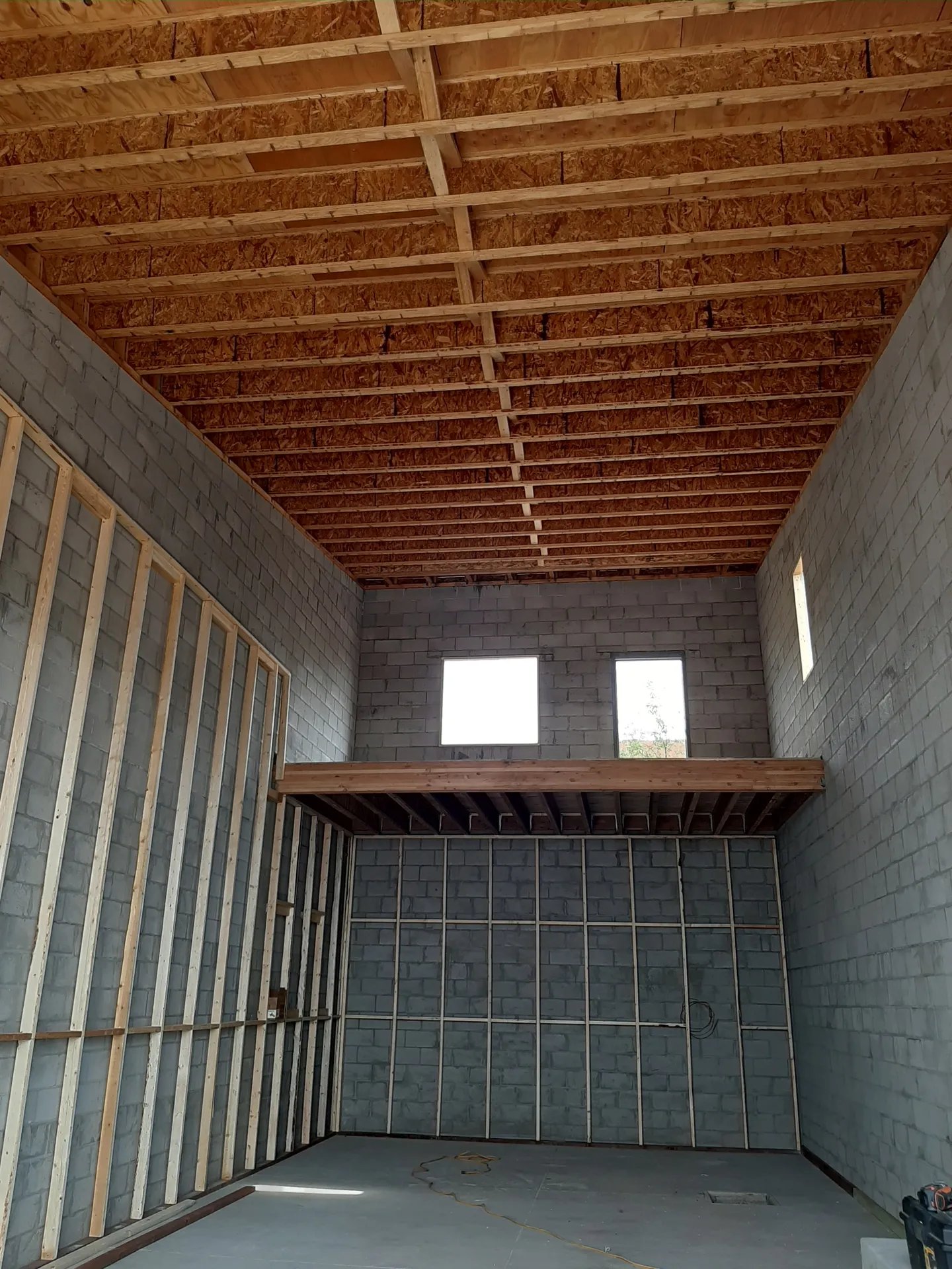 Unfinished interior with wooden roof trusses and concrete block walls