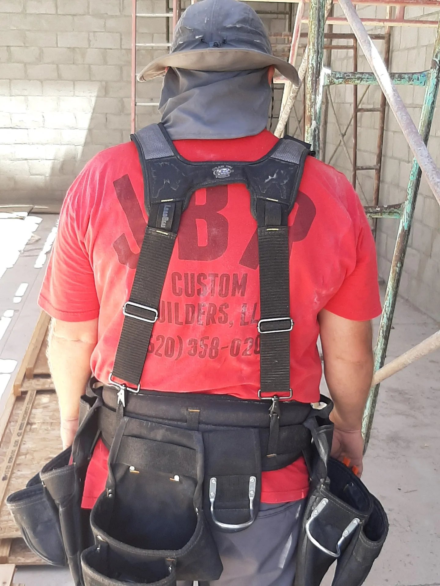 Construction worker in red shirt with tool belt and suspenders on job site