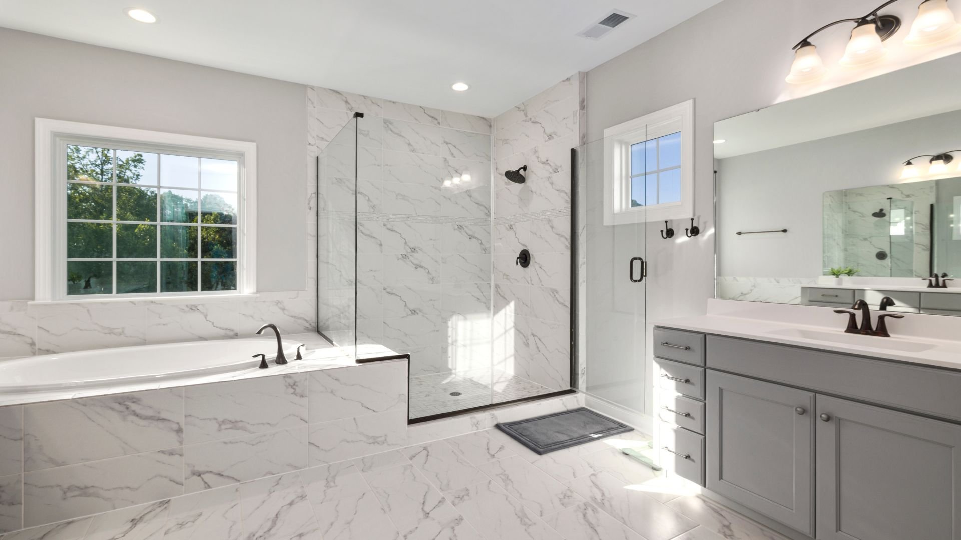 Luxurious marble bathroom with glass shower, bathtub, and gray vanity