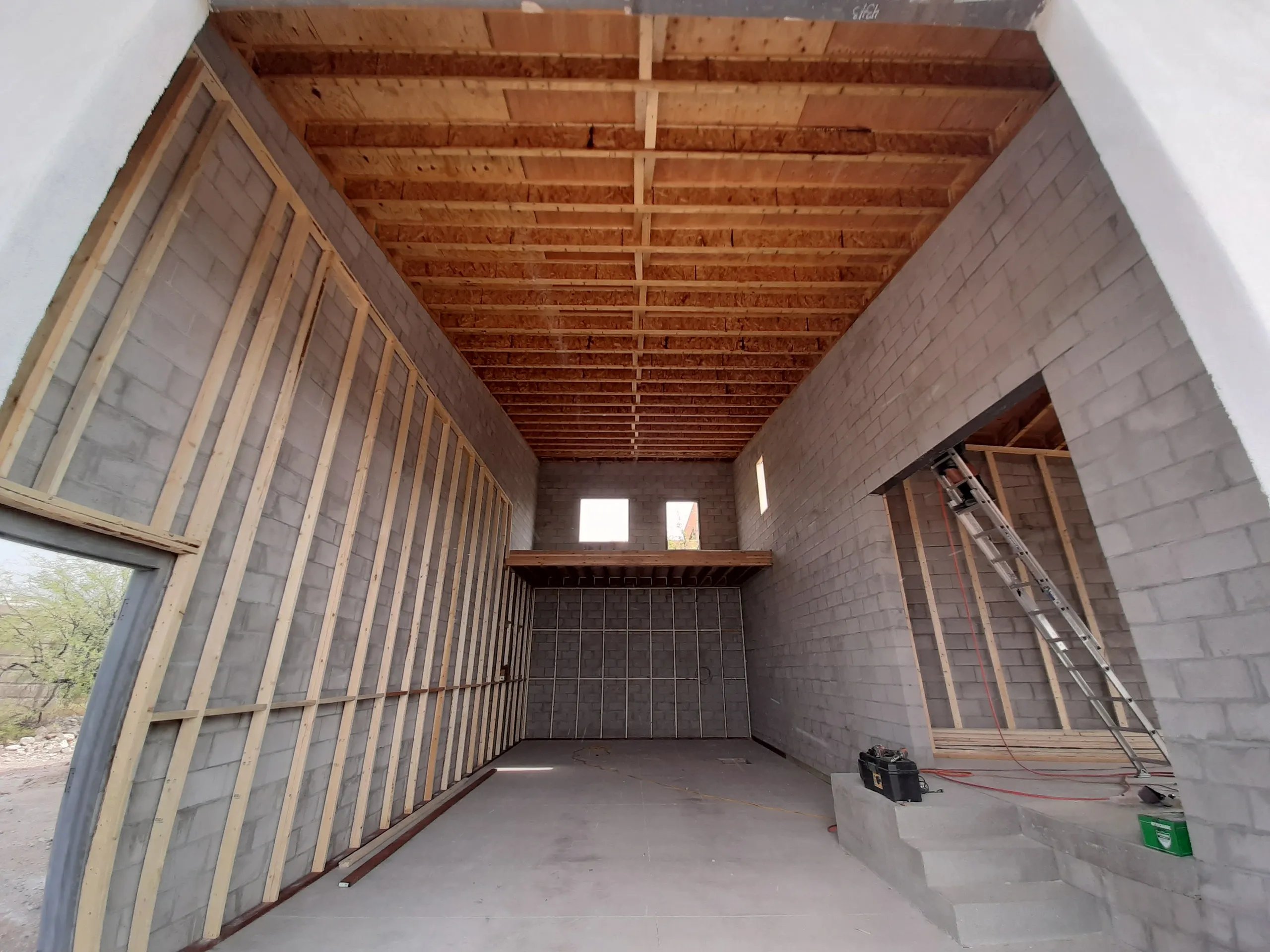 Unfinished interior of building with concrete walls and wooden roof framing