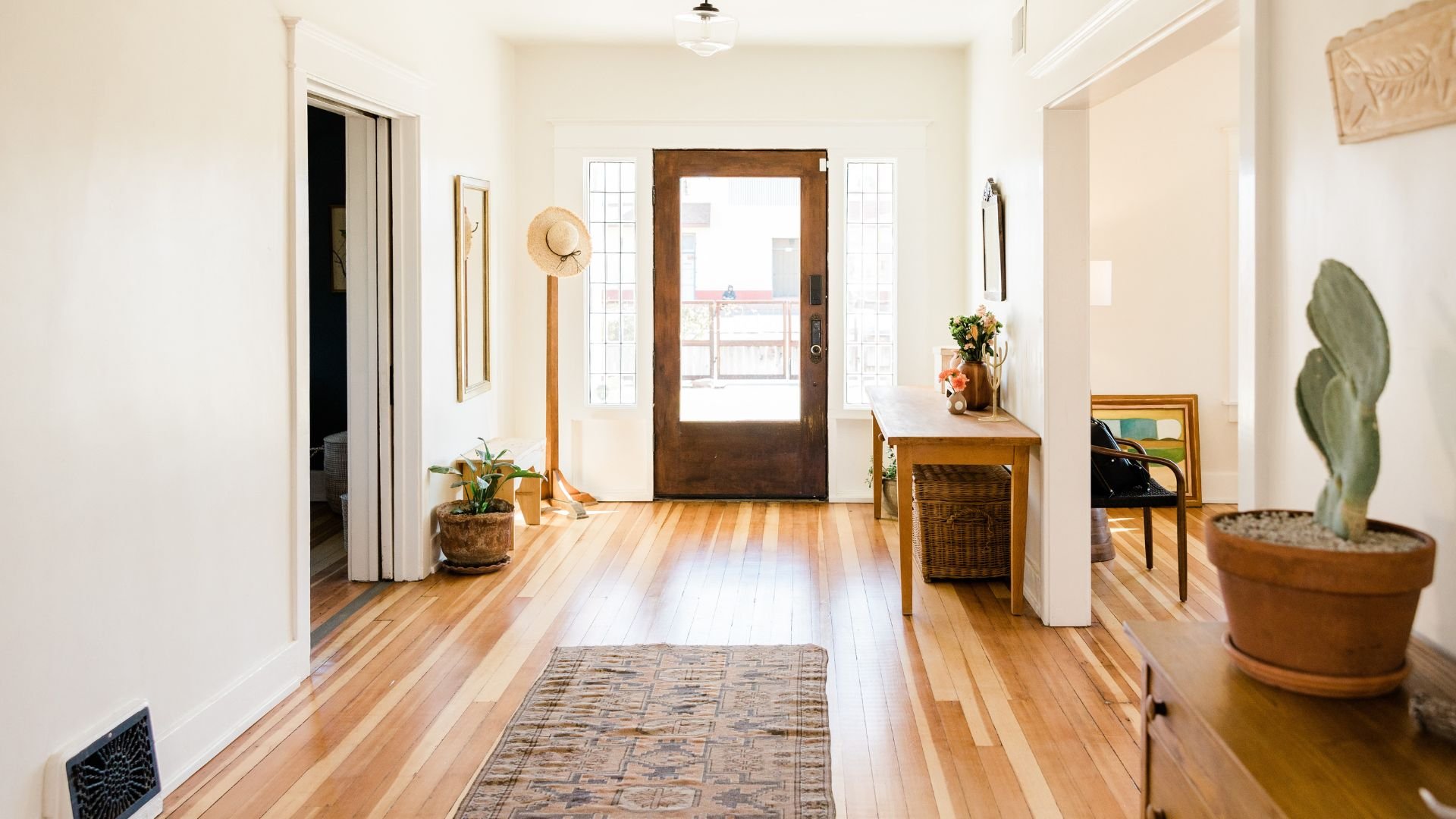 Bright entryway with wooden door, plants, rug, and natural light